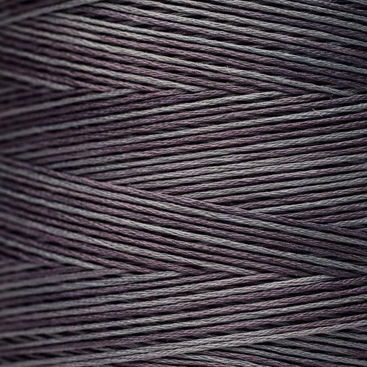 A close-up texture shot of multi-ply thread wound in a cone, showing fine strands twisted into dark purple and gray threads.