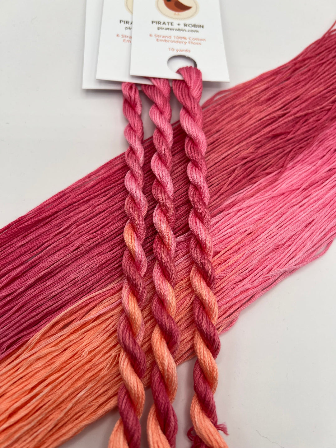 twisted skeisn of thread in pink and orange colors with a visible brand tag on a light background