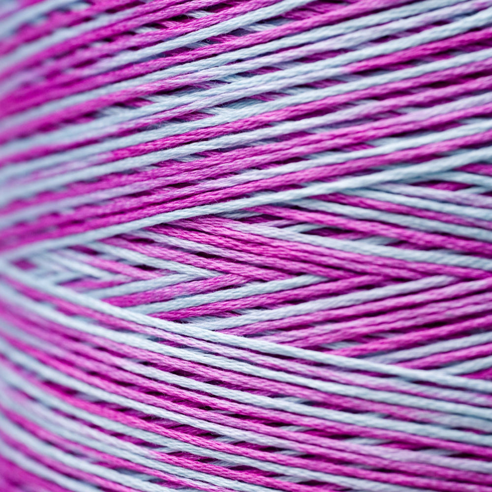A close-up of variegated thread wound in a cone, showing alternating strands of bright magenta pink and light lavender-gray.