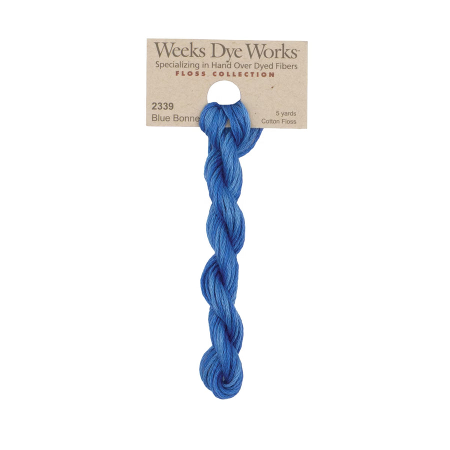 A skein of Weeks Dye Works Blue Bonnet cotton floss, displayed on its original kraft paper hanger card against a plain white background.