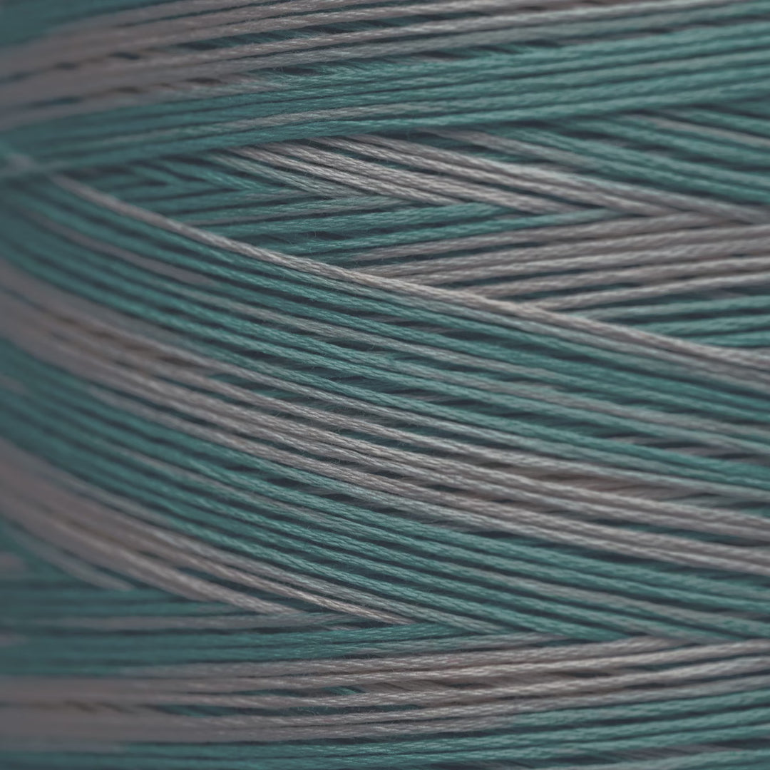 A close-up of variegated yarn strands in teal and light gray, arranged diagonally.