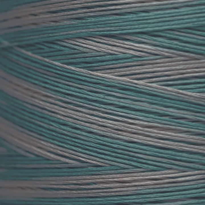 A close-up of variegated yarn strands in teal and light gray, arranged diagonally.