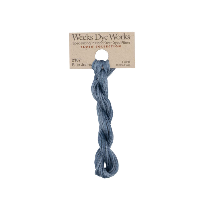 A skein of Weeks Dye Works Blue Jeans cotton thread in a dusty blue shade, attached to its original kraft paper label.