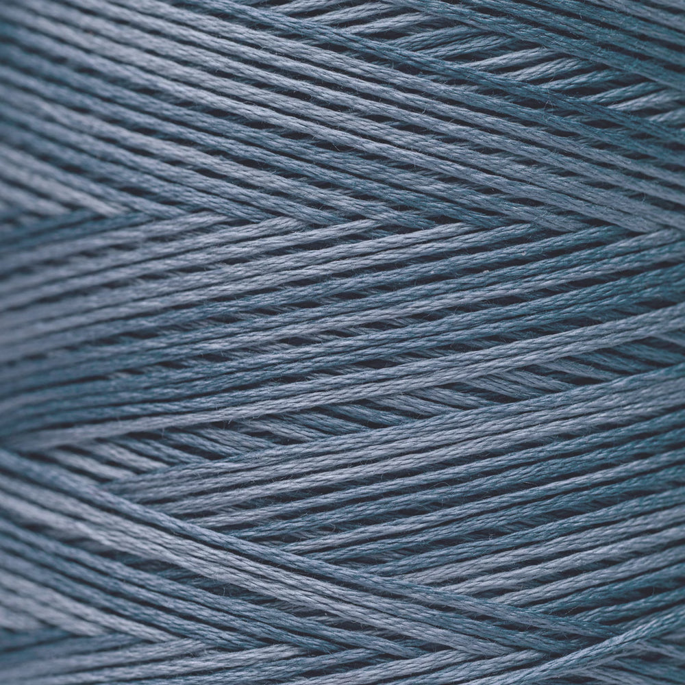 A close-up texture shot of fine yarn strands wound in a herringbone pattern, showing a dusty slate blue color.