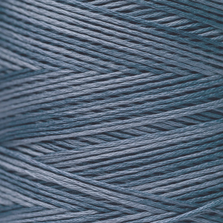 A close-up texture shot of fine yarn strands wound in a herringbone pattern, showing a dusty slate blue color.