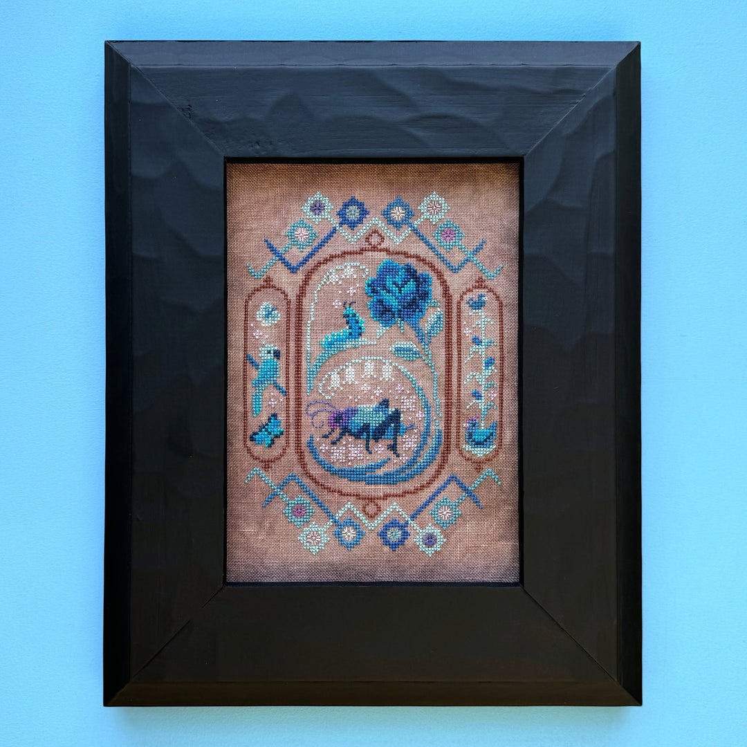 Framed cross-stitched artwork with decorative elements on a blue background