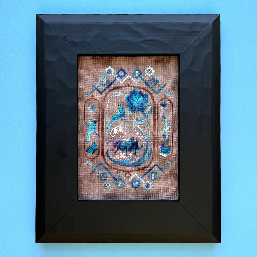 Framed cross-stitched artwork with decorative elements on a blue background