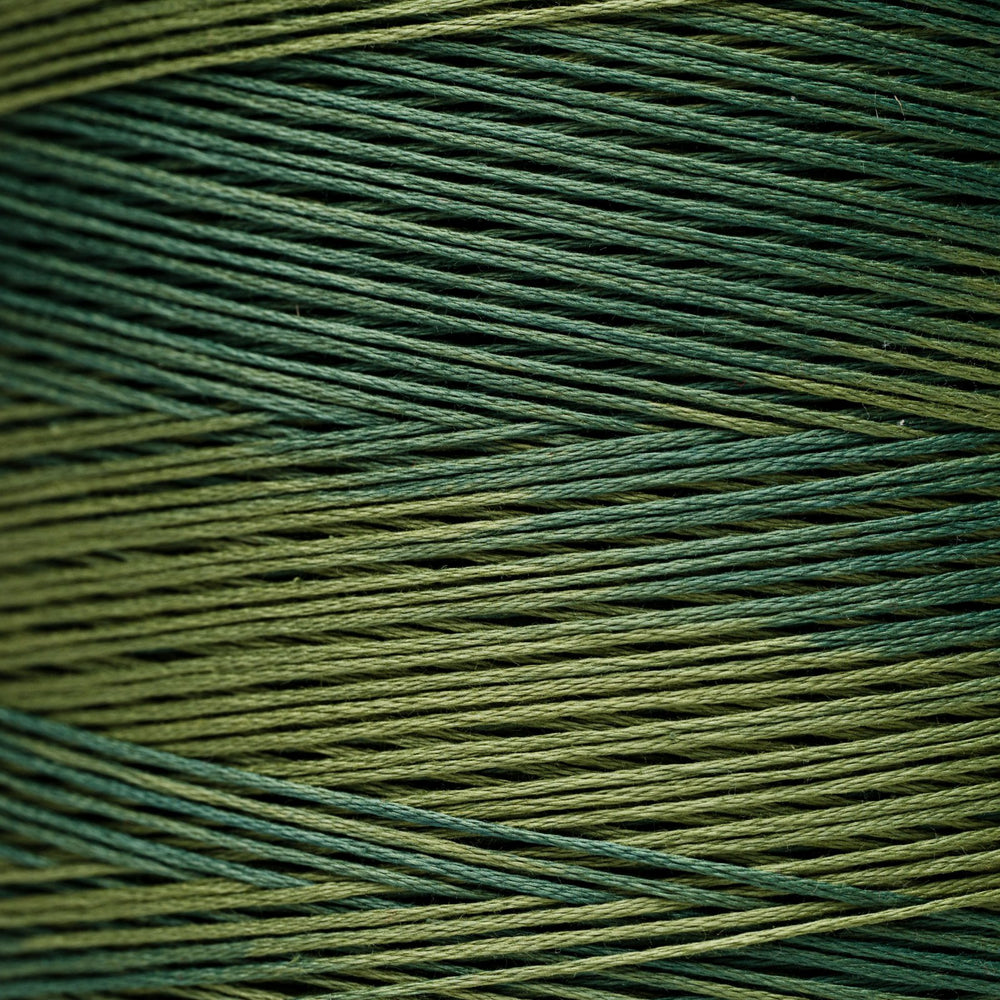 A close-up of tightly wound yarn or thread strands in a variegated colorway of forest green and olive green.