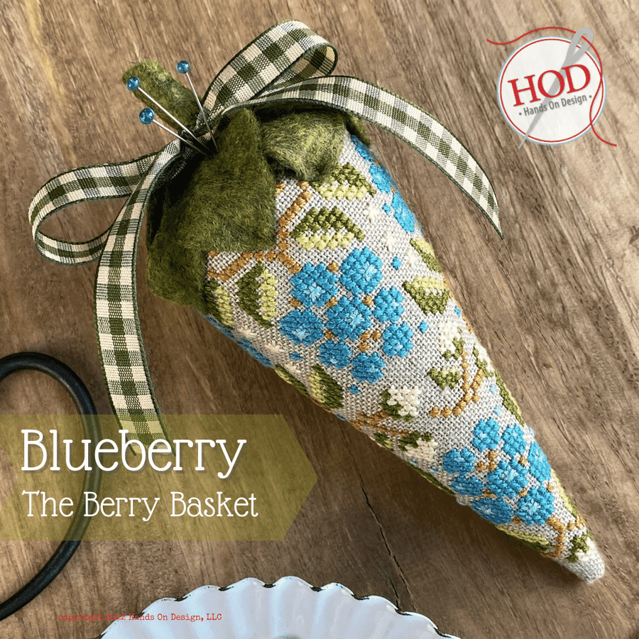 Decorative blueberry-shaped basket with a checkered ribbon on a wooden surface, featuring the brand 'HOD'.
