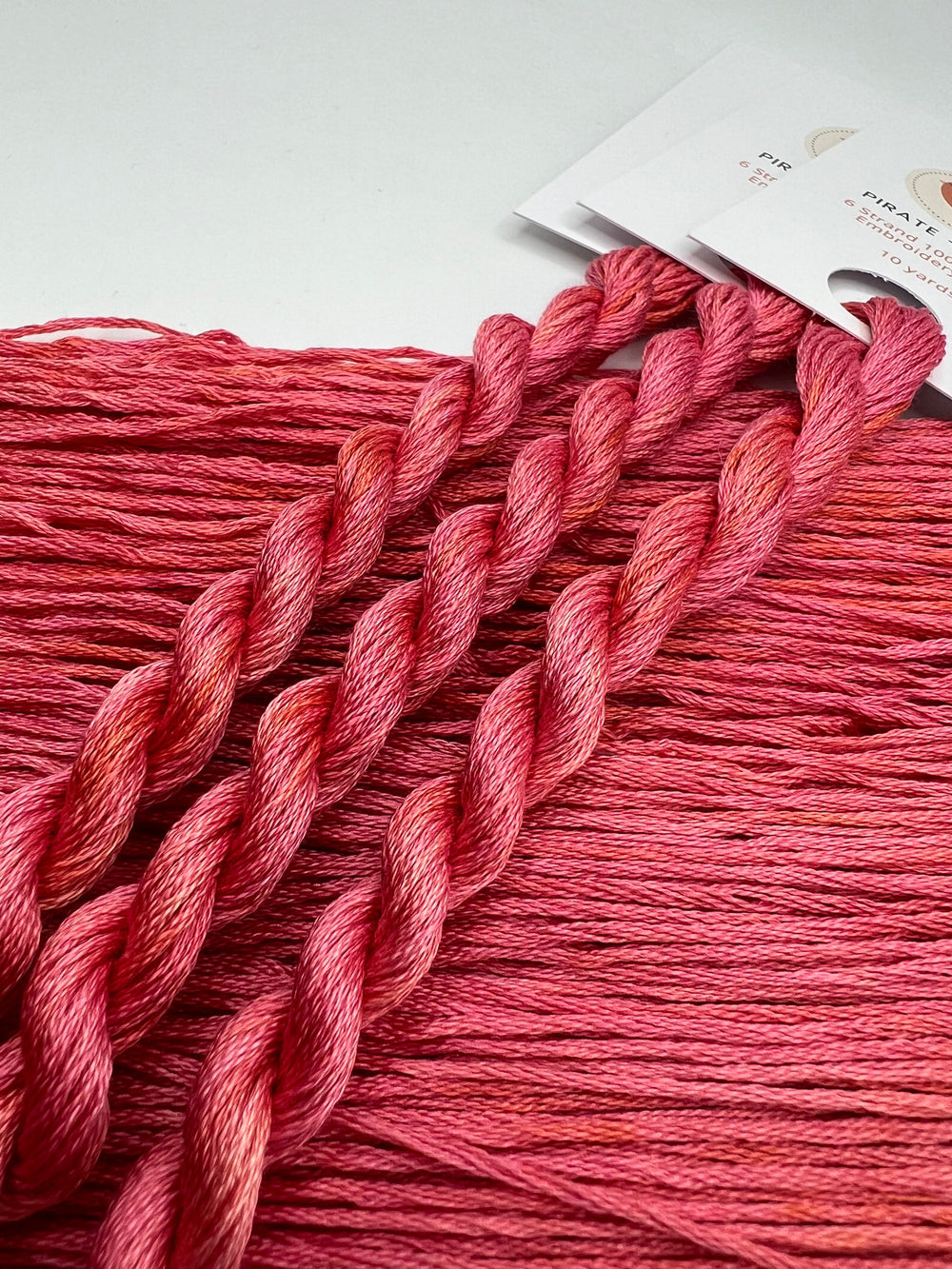 Close-up of pink embroidery floss with a spool in the background on a light gray surface.