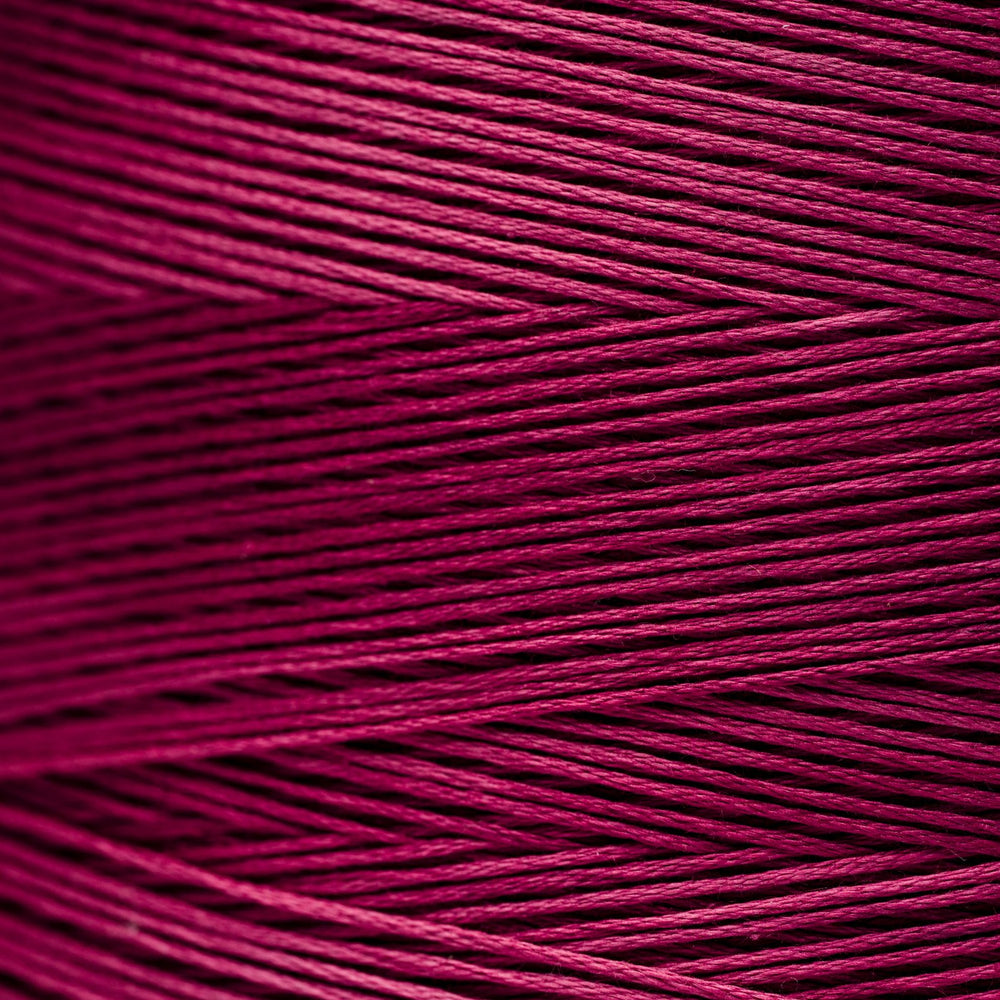 A close-up of tightly wound fuchsia magenta thread showing the texture and color of the material.