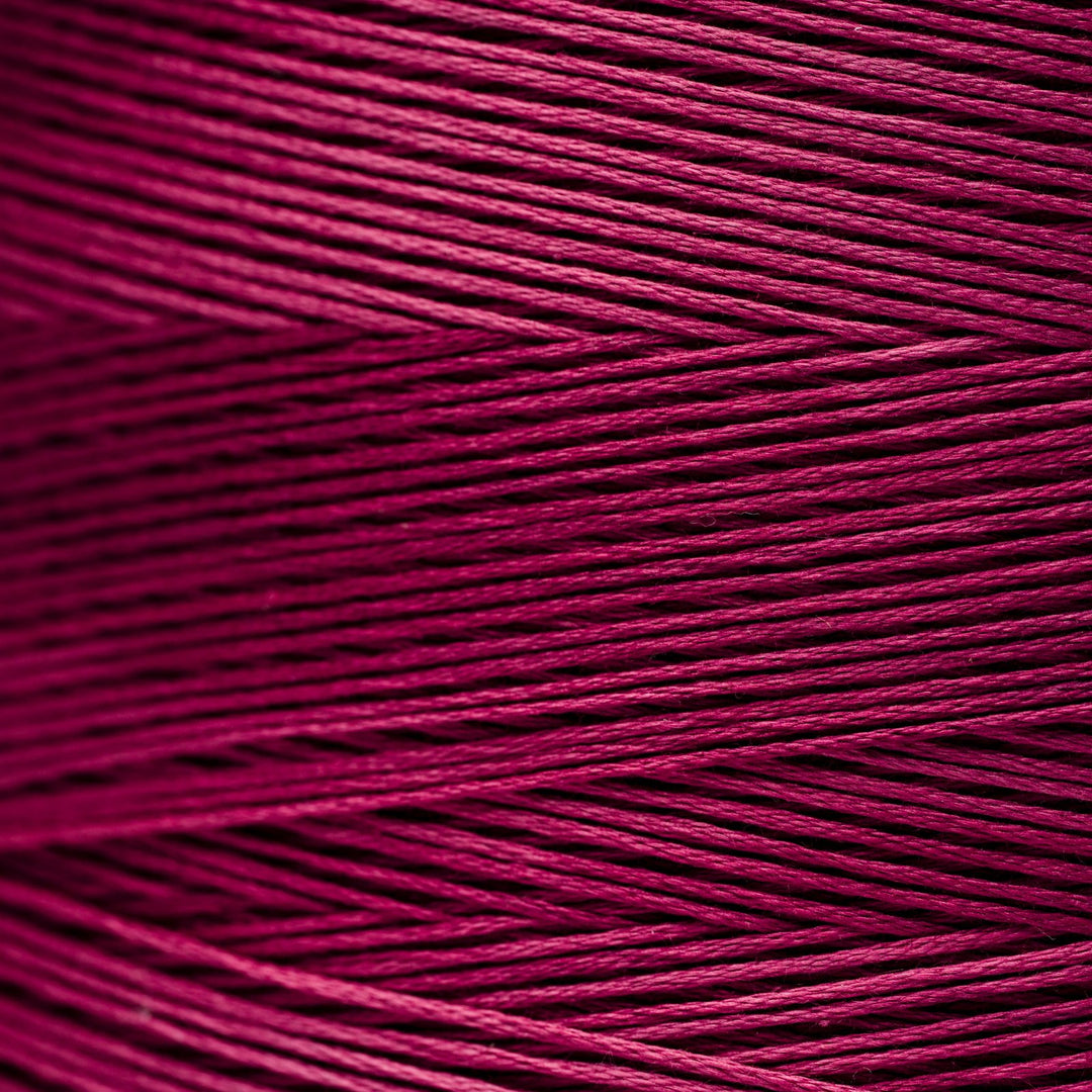 A close-up of tightly wound fuchsia magenta thread showing the texture and color of the material.