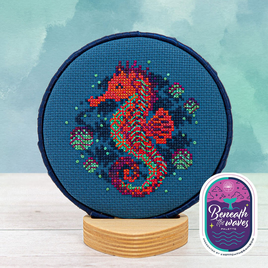 Cross-stitched seahorse design on a hoop with a 'Beneath the Waves' palette label.