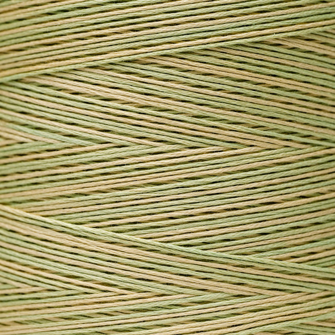 A close-up of tightly wound thread in a two-tone pattern of sage green and light tan, arranged in a herringbone texture.