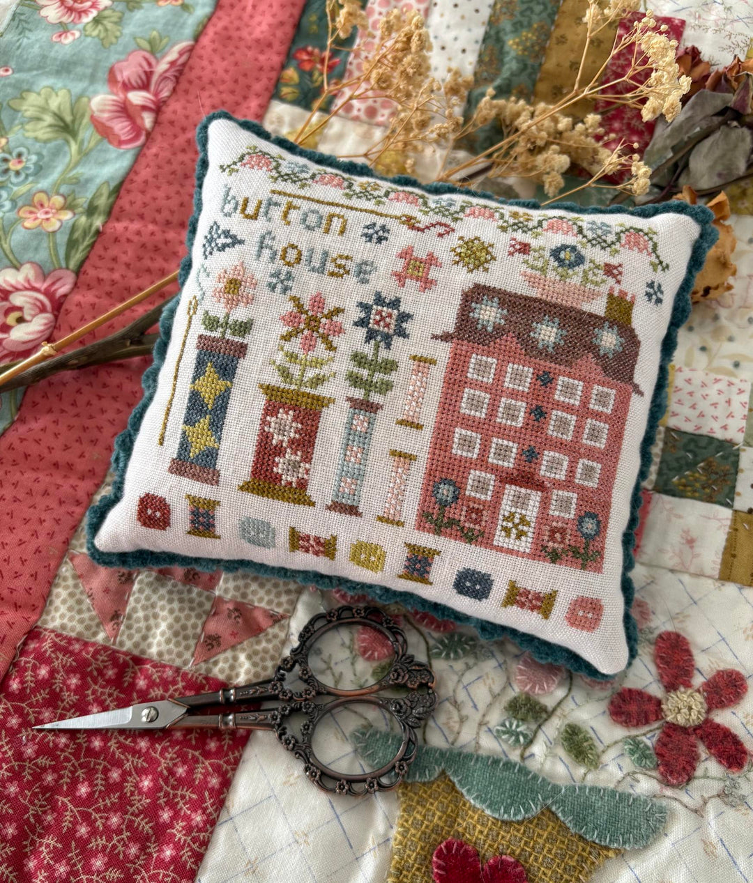Decorative pillow with cross-stitch design on a quilt with scissors and flowers.