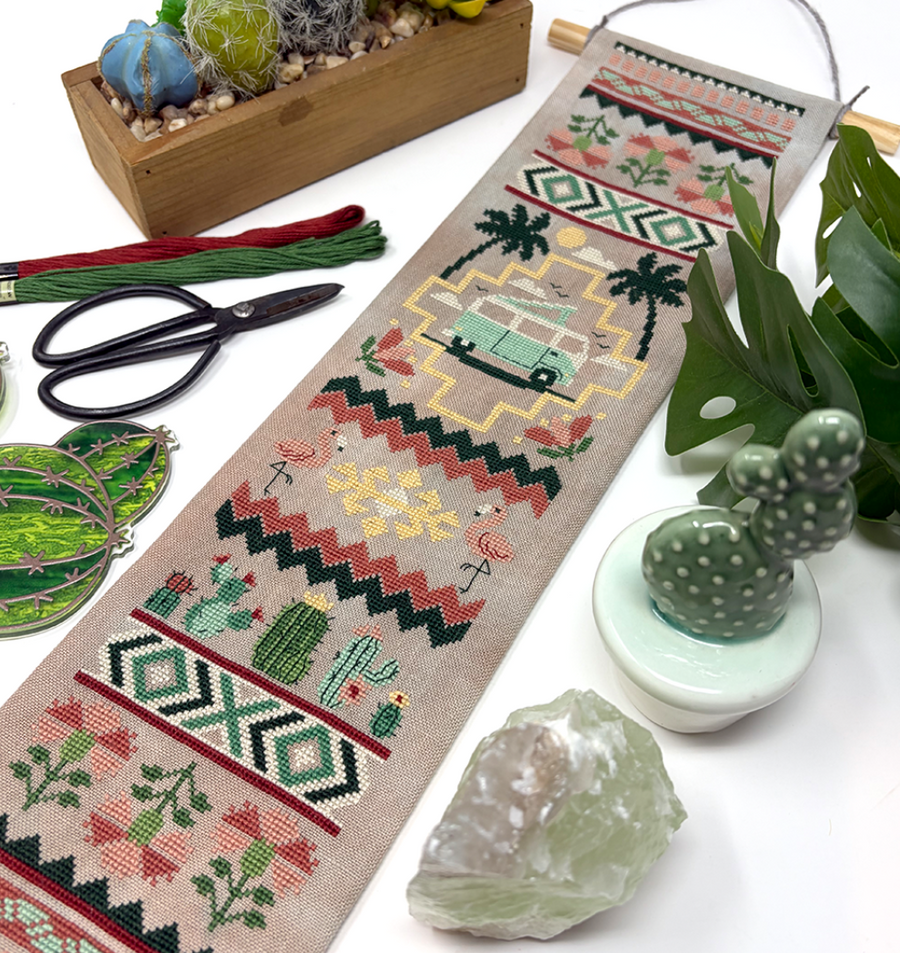 Cactus and caravan bell pull with embroidery design on a white surface with plants and tools.