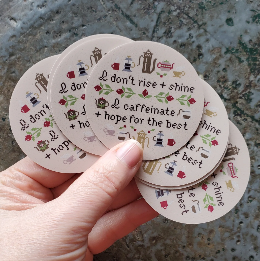 Stack of round stickers with text and coffee graphics held by a hand on a textured surface.