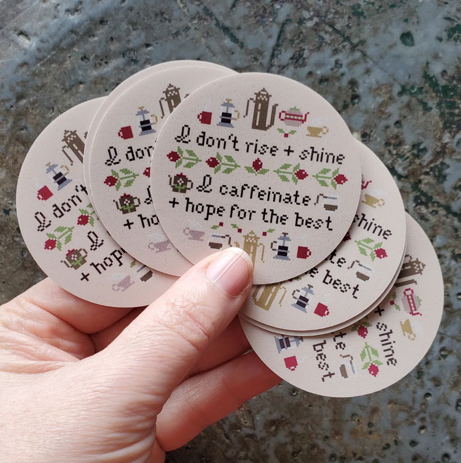 Stack of round stickers with text and coffee graphics held by a hand on a textured surface.