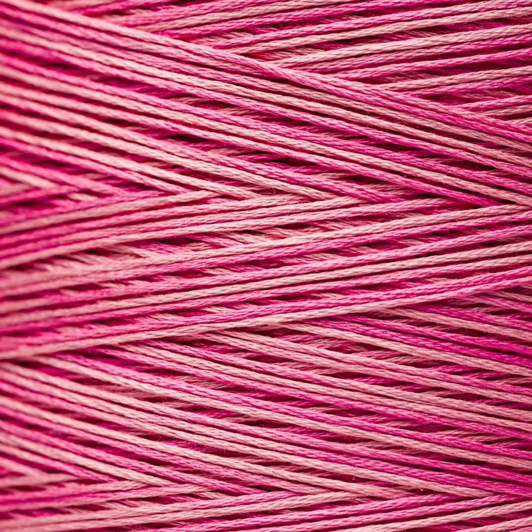A close-up texture shot of pink and magenta variegated embroidery thread wound in diagonal layers.