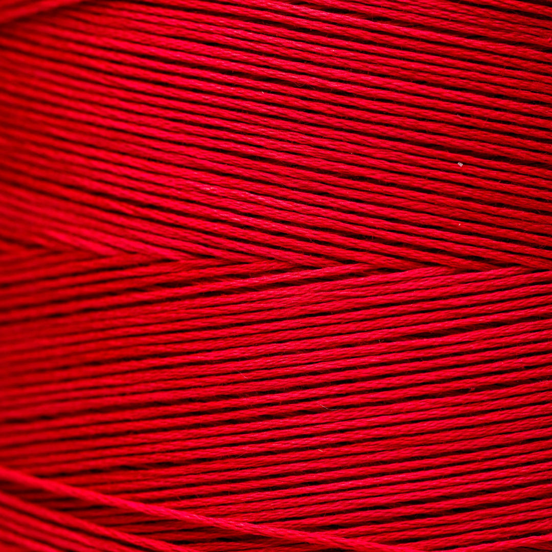 A close-up of bright red yarn or thread wound in horizontal layers, filling the entire frame.