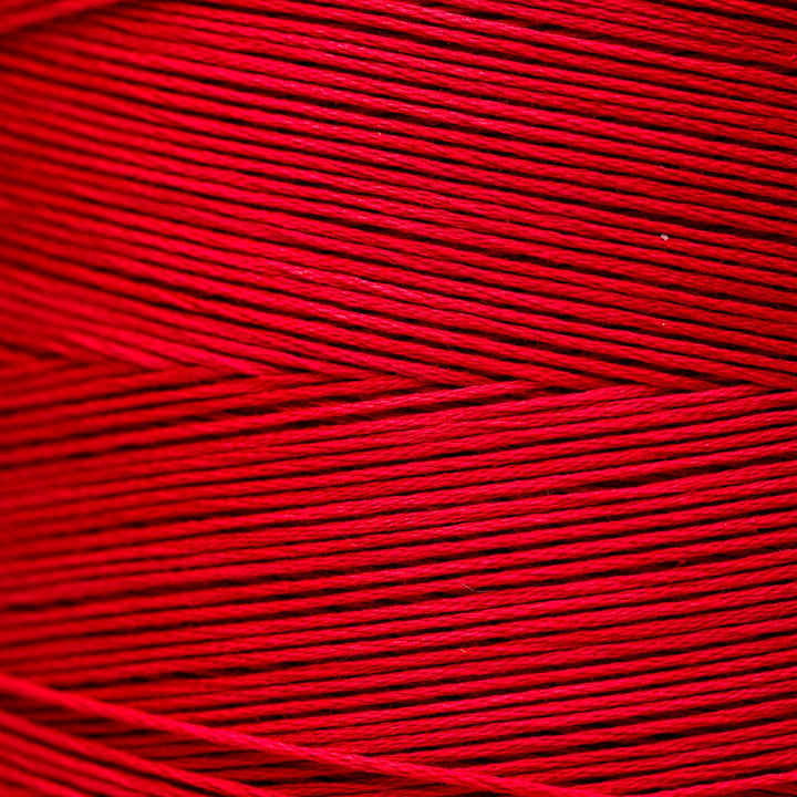 A close-up of bright red yarn or thread wound in horizontal layers, filling the entire frame.