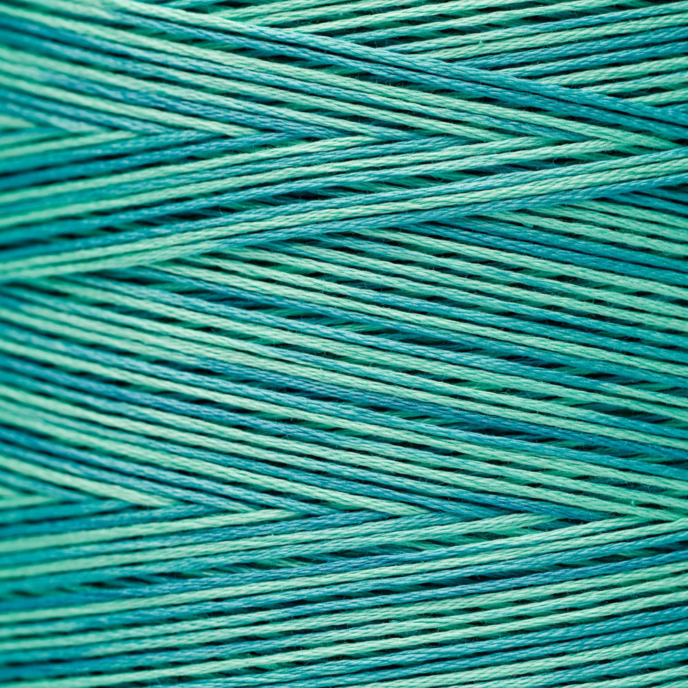 A close-up of teal and turquoise braided cord or thread filling the frame, showing the texture and color variation.