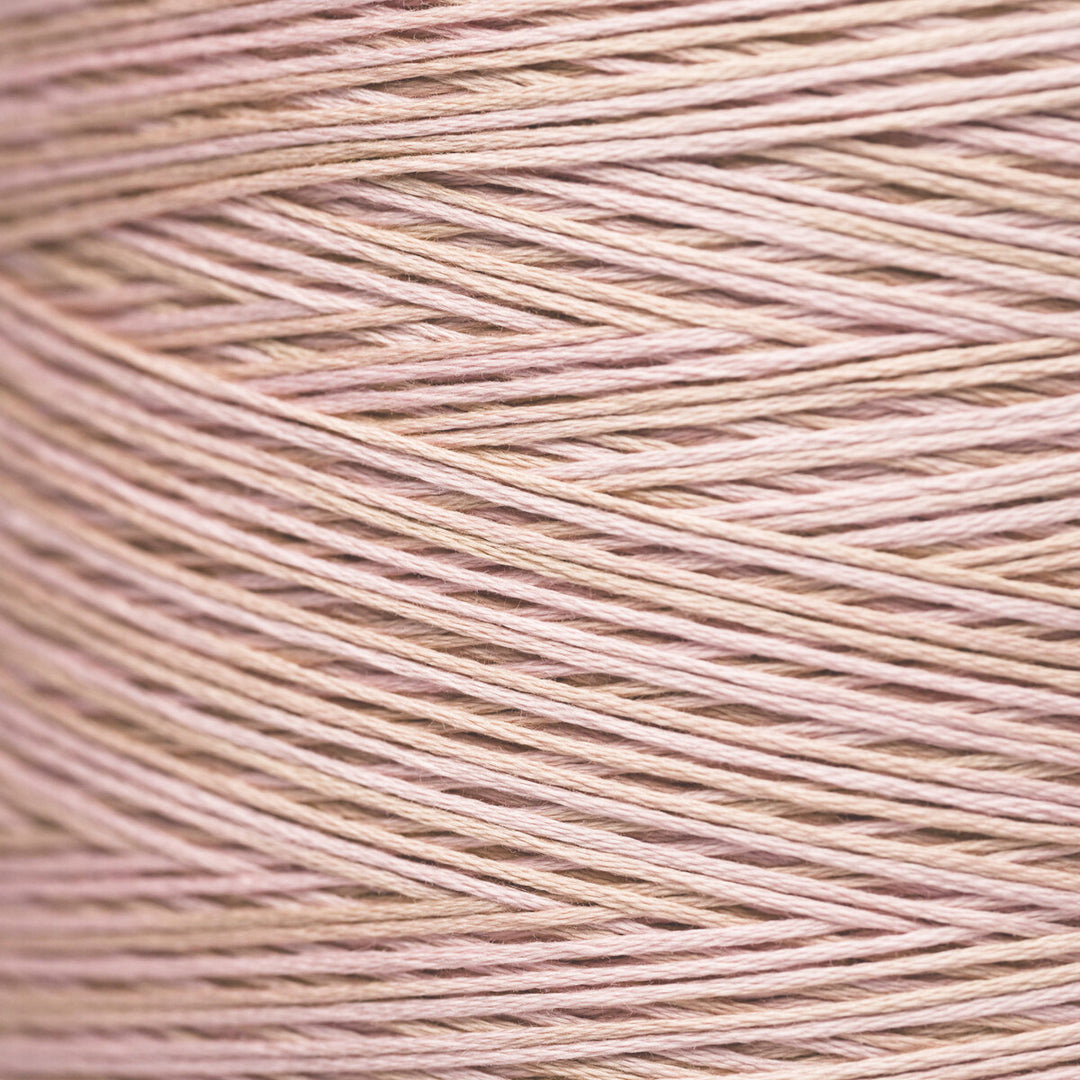 A close-up texture shot of fine yarn wound in a cone, showing the fine strands in a soft dusty pink color.