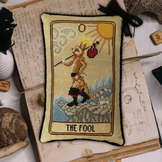 Decorative pillow with tarot card design titled 'The Fool' on an open book.