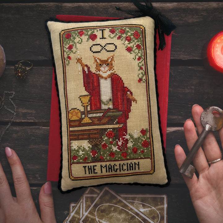 Cross-stitched pillow featuring 'The Magician' from a tarot card design on a wooden surface.