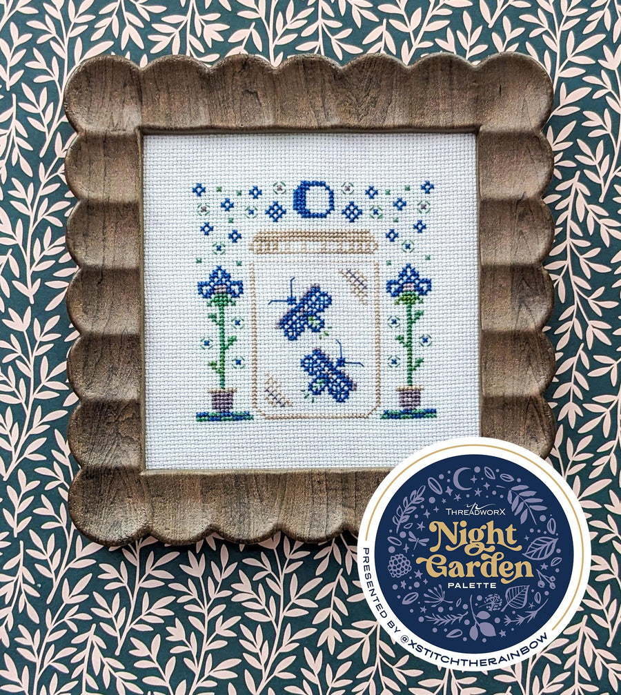 Cross-stitched design of a garden scene with a wooden frame on a patterned background, featuring the 'Night Garden Palette' brand.