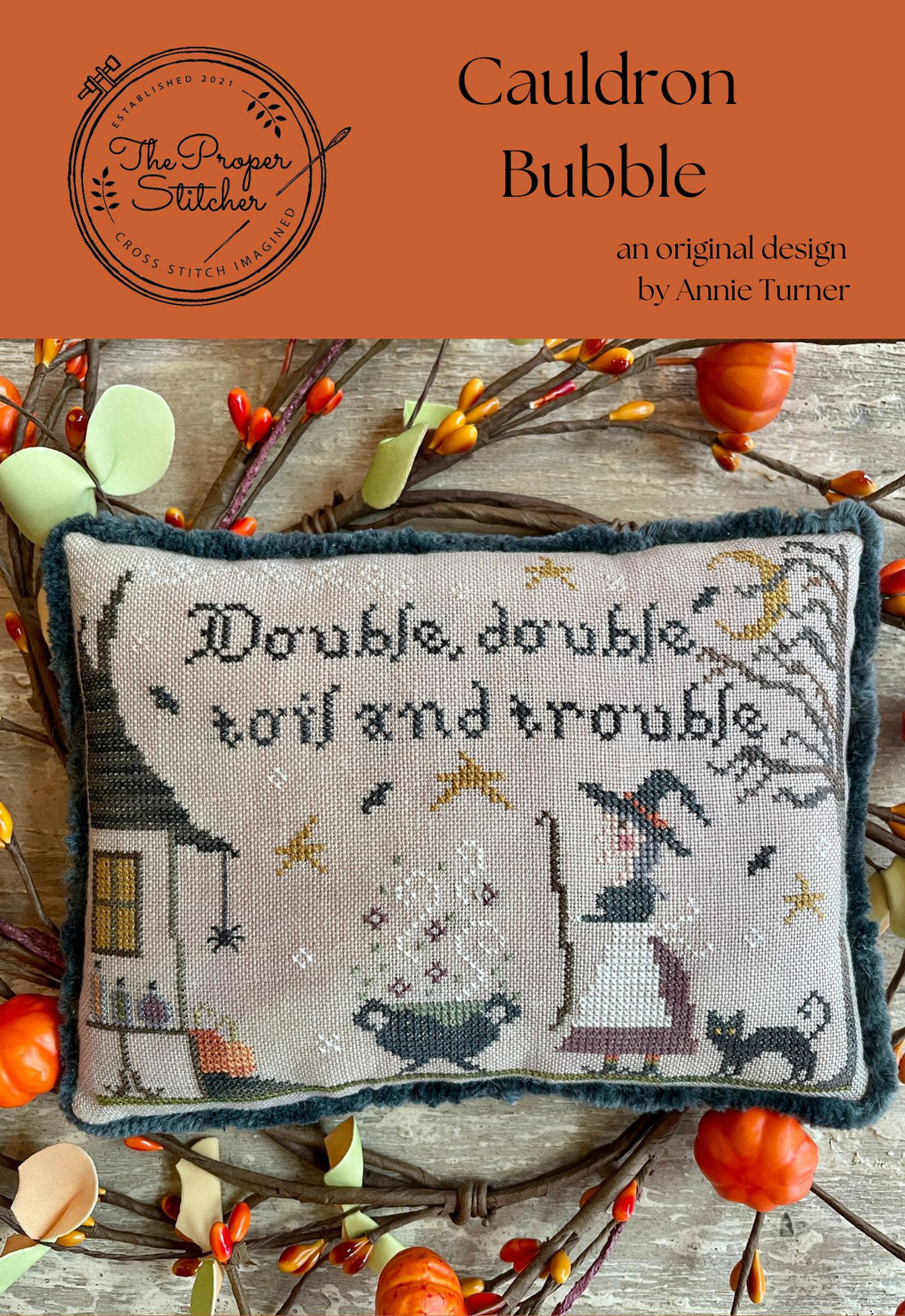 Cross-stitched pillow with 'Double, double toil and trouble' text and Halloween-themed design, surrounded by autumn leaves and pumpkins.