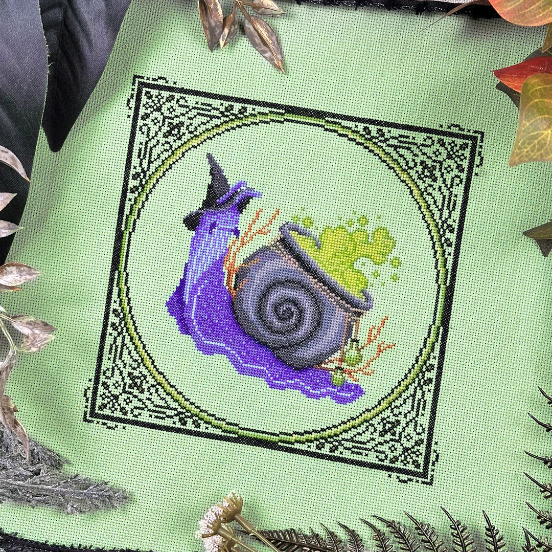 Embroidered design of a purple witch hat and green broomstick on a green fabric background.