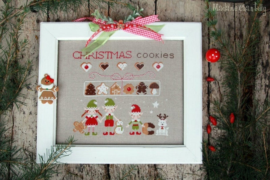 Framed Christmas-themed cross-stitch art with decorative elements on a wooden background.