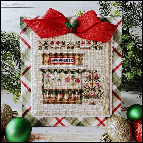 Decorative cross-stitched ornament with a red bow and Christmas-themed design on a plaid background.