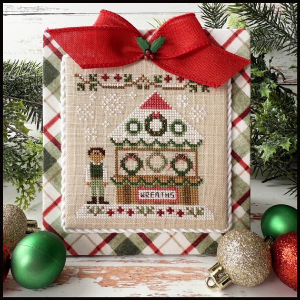 Cross-stitched Christmas scene with wreaths and a red bow, surrounded by festive decorations.
