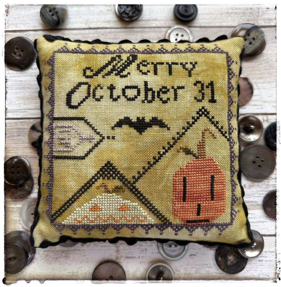Cross-stitched pillow with 'Merry October 31' text and Halloween-themed design on a wooden surface with buttons.
