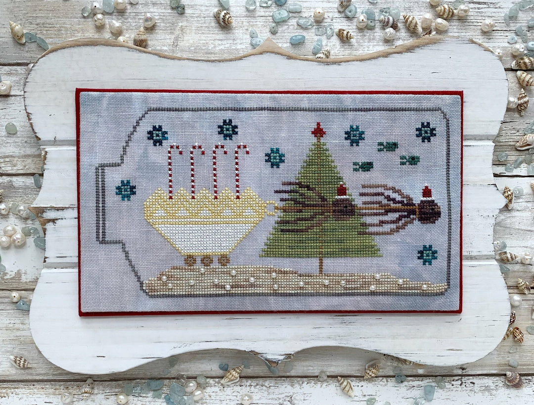 Decorative cross-stitched scene with Christmas elements on a wooden background.