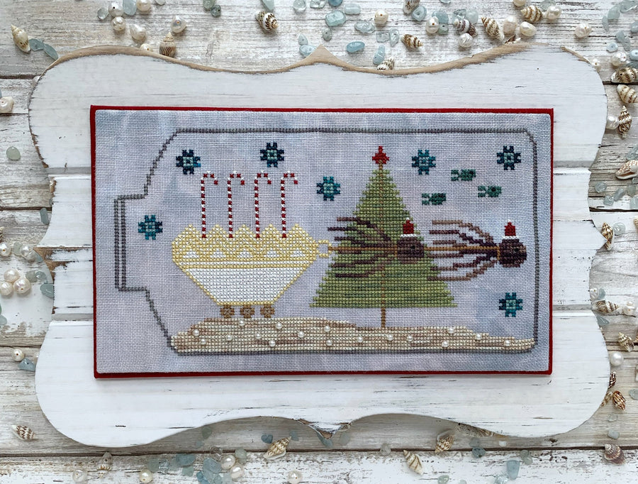 Decorative cross-stitched scene with Christmas elements on a wooden background.