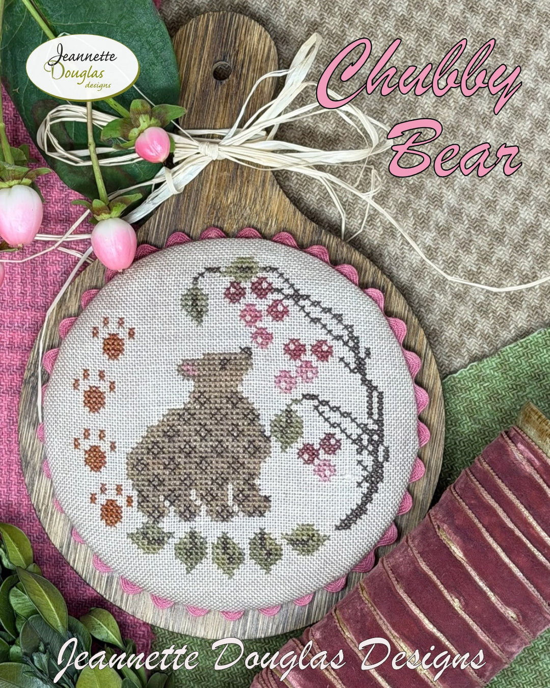 Cross-stitched round design featuring a bear surrounded by flowers and leaves, with 'Jeannette Douglas Designs' branding.
