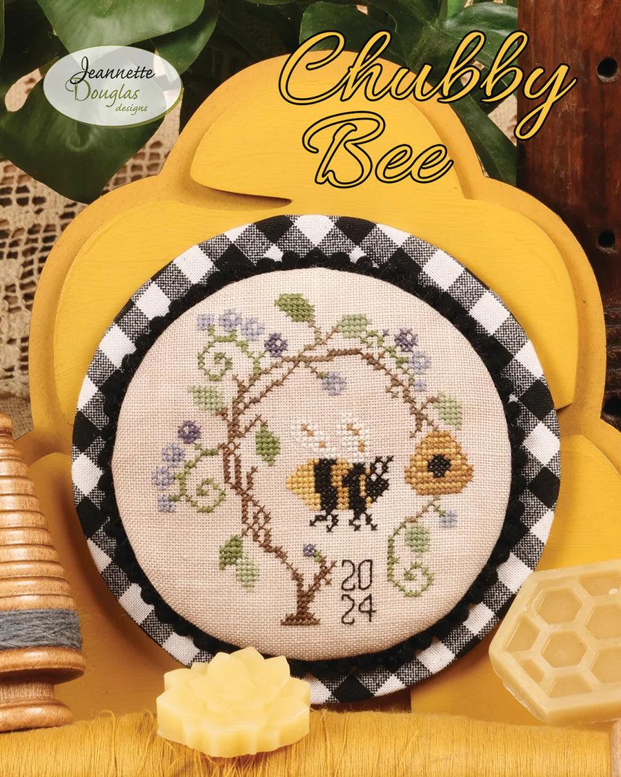 Cross-stitched bee design with floral elements on a checkered border, set against a yellow background.
