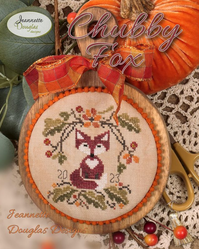 Cross-stitched fox design in a wooden hoop with autumn-themed decorations.