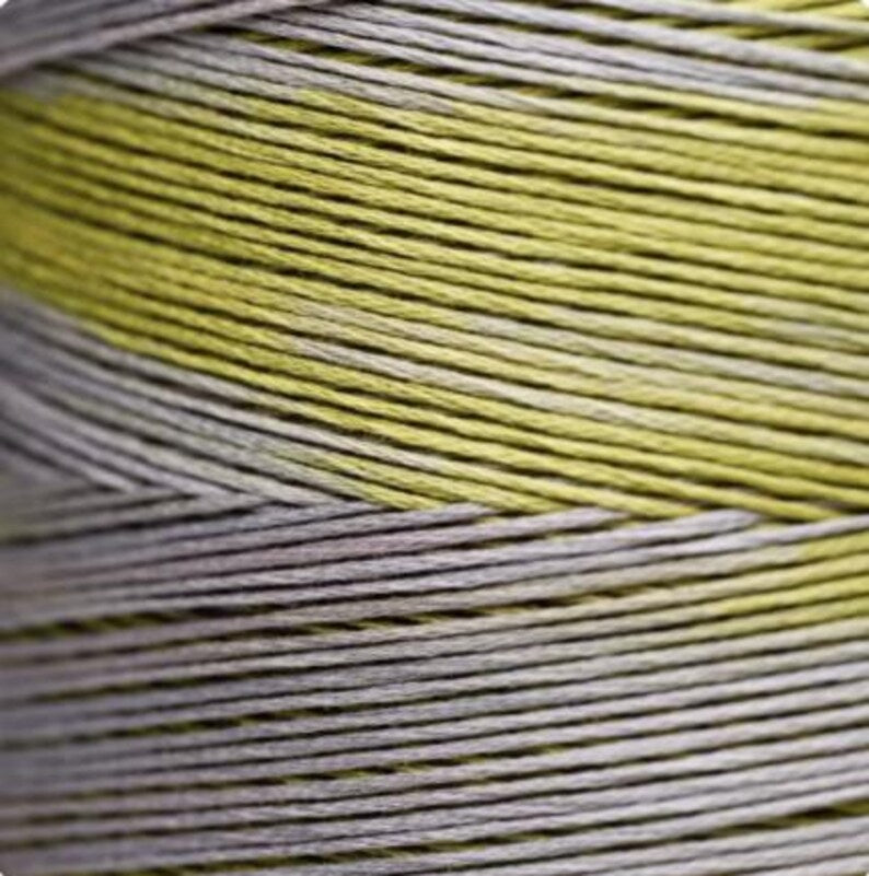 A close-up of tightly wound thread strands showing a color-shifting pattern with alternating bands of pale yellow-green and light gray.