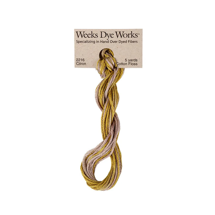 A skein of Weeks Dye Works cotton embroidery floss in a mustard yellow and dusty lavender-gray blend, attached to its original kraft paper label.
