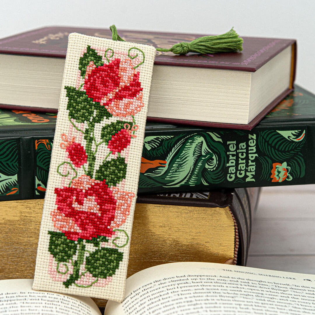Cross-stitched bookmark with red roses on a stack of books