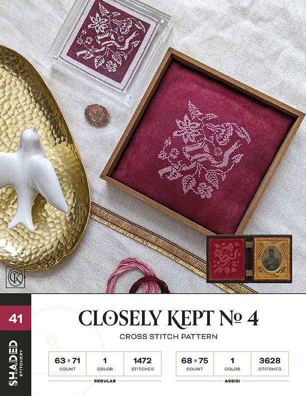 A cross stitch pattern named 'Closely Kept No. 4', featuring a shaded floral design on a purple fabric, displayed alongside a needle and floss, indicating a do-it-yourself craft kit.