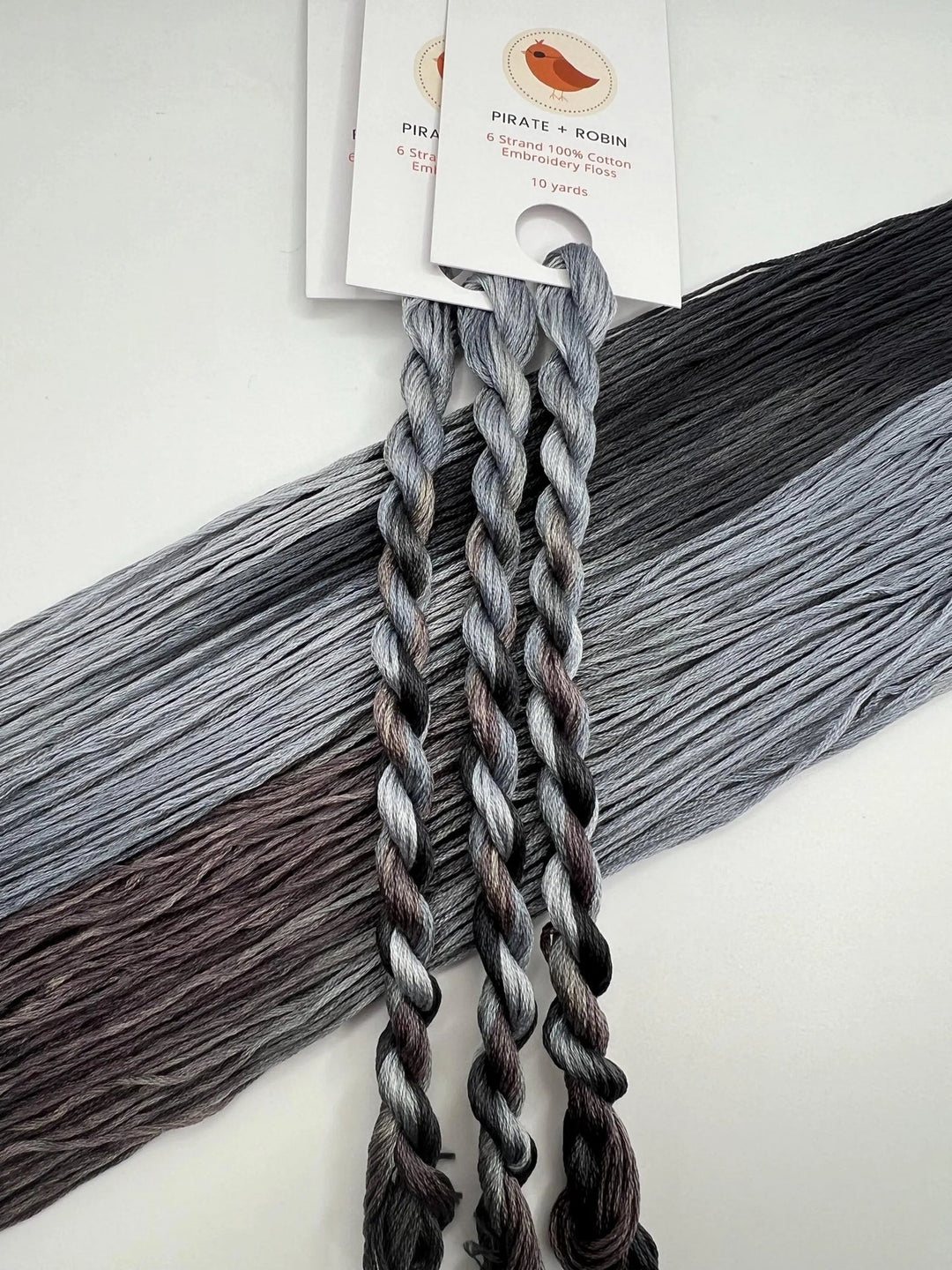 light and dark Gray thread skeins with a brand label on a light background