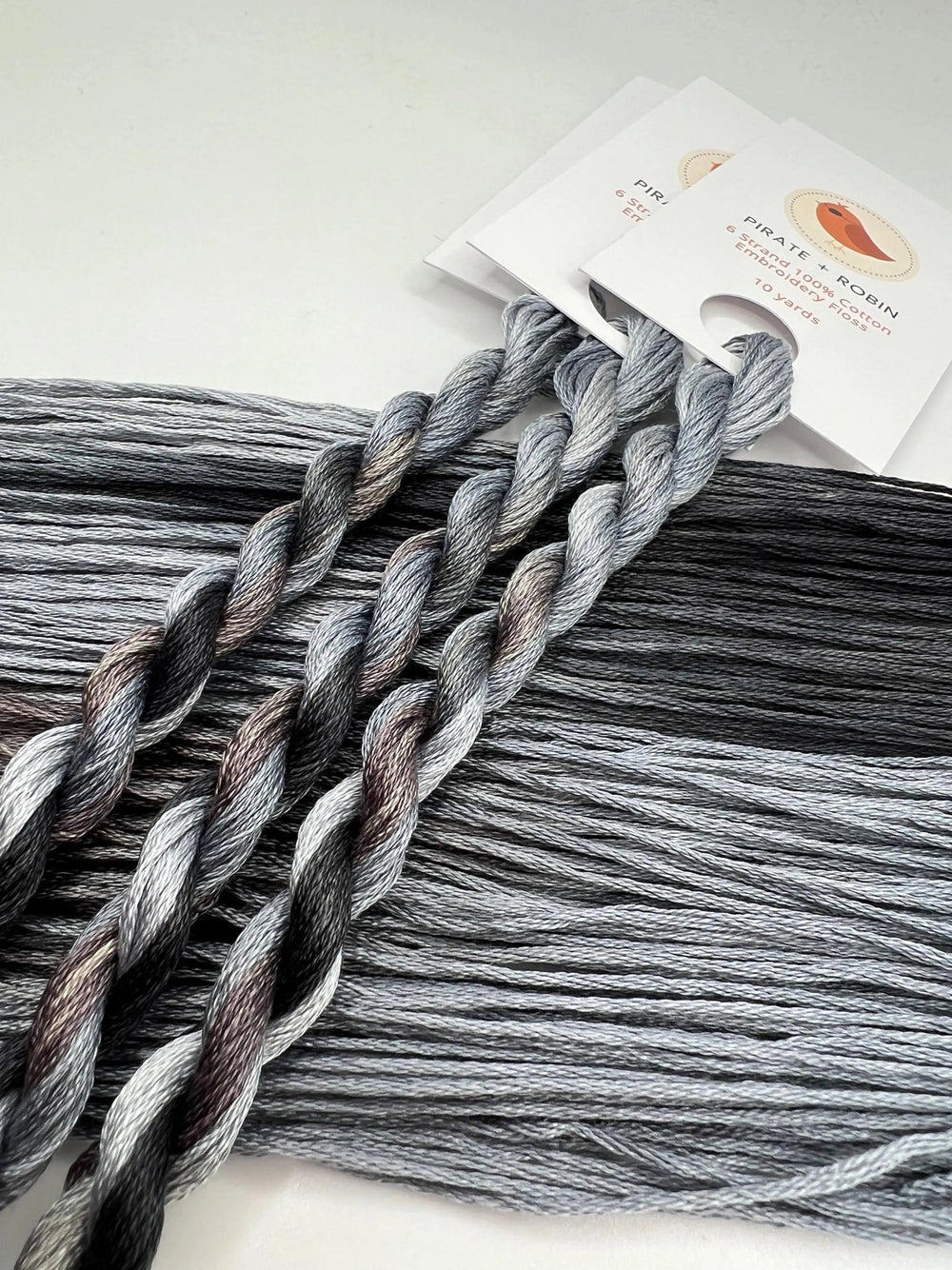 light and dark Gray thread skeins with a brand label on a light background