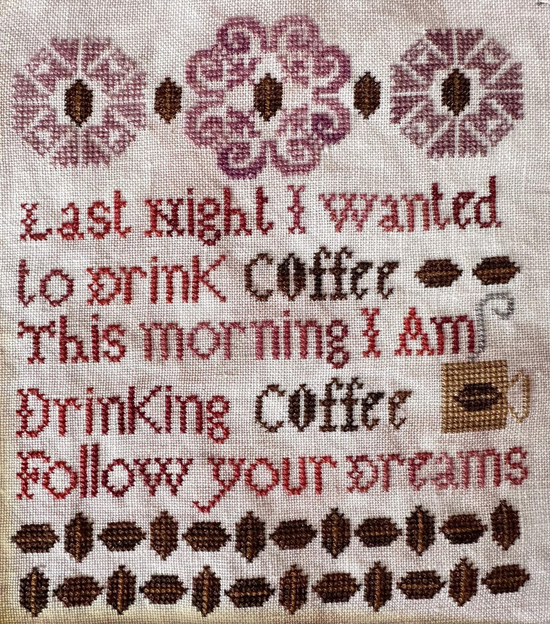 Cross-stitched text on fabric with coffee-themed design