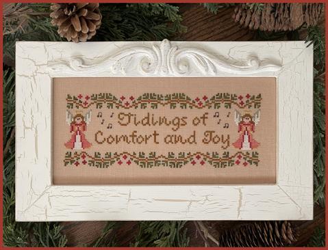 Framed cross-stitched design with 'tidings of Comfort and Joy' text and angel illustrations, surrounded by greenery.