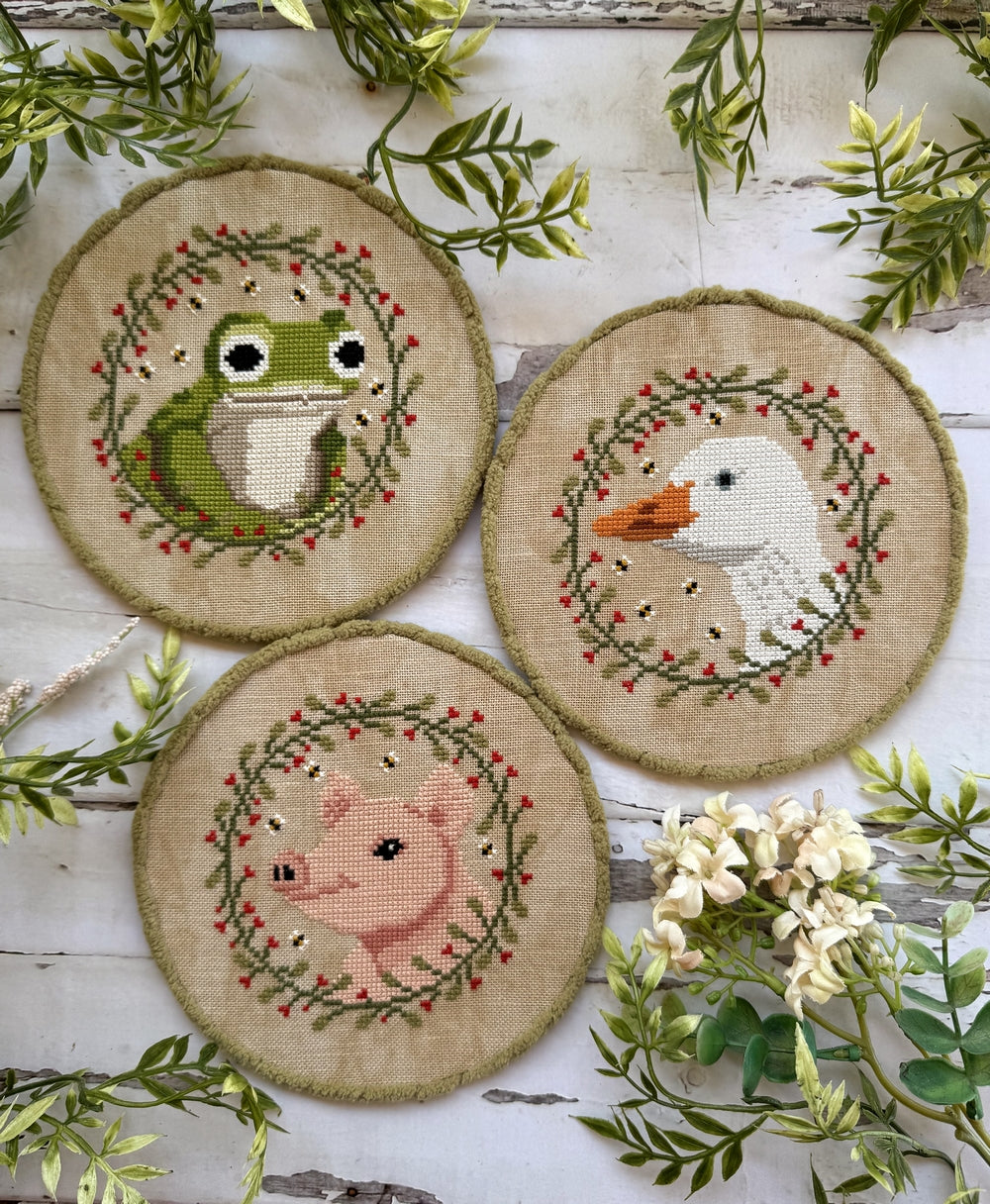 Three embroidered ornaments with animal designs on a wooden surface with greenery.